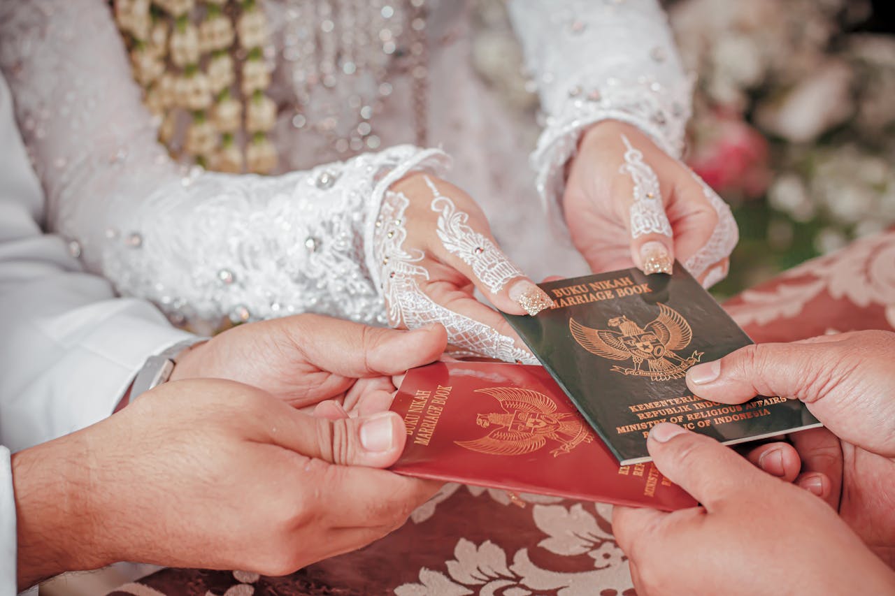 Close-up of hands exchanging Indonesian marriage books during a wedding ceremony.