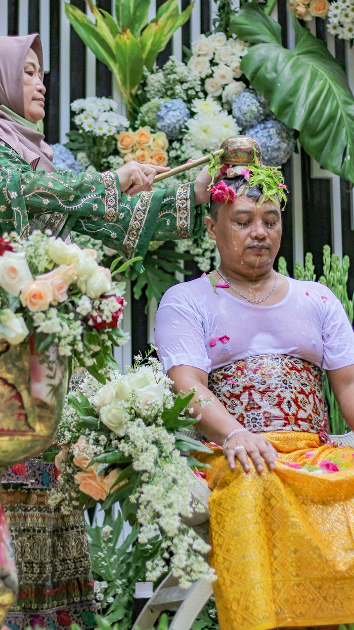 A colorful traditional ceremony with floral decor, featuring a man receiving water on his head.