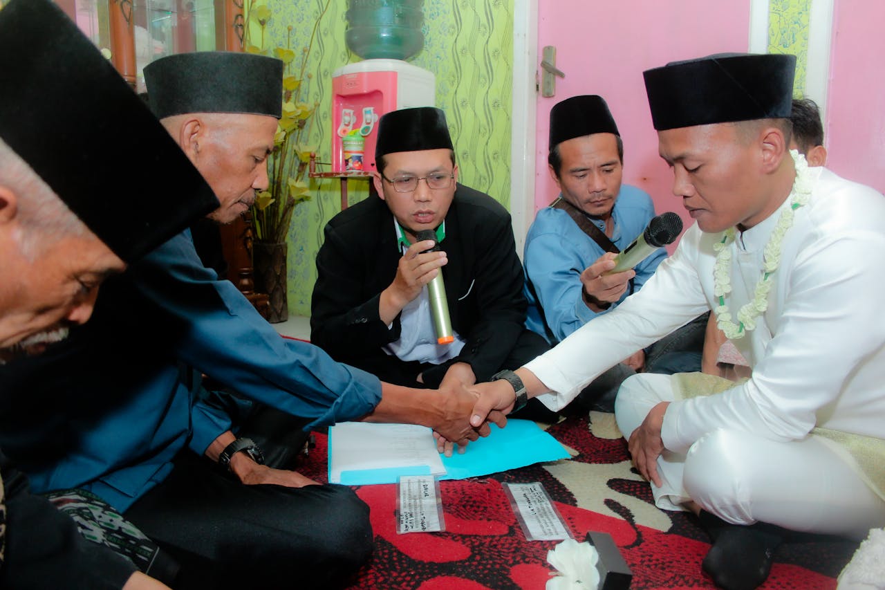 Men participating in a traditional ceremony, wearing cultural attire and holding microphones.