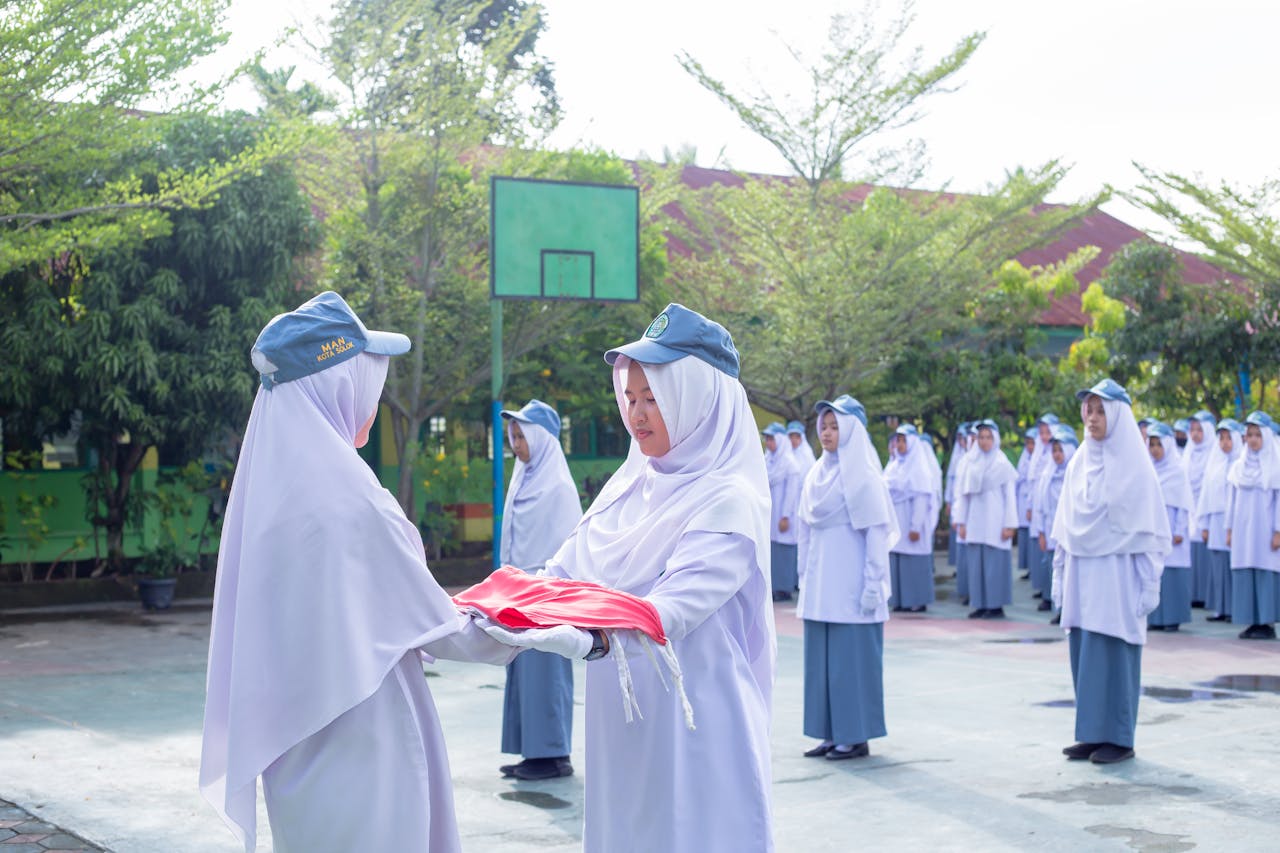 Students in uniforms perform a flag ceremony on a sunny day outdoors.